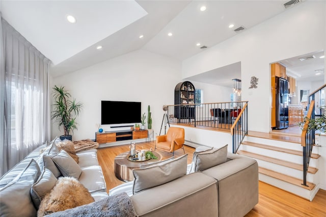 living room featuring light wood-type flooring, visible vents, vaulted ceiling, and stairs