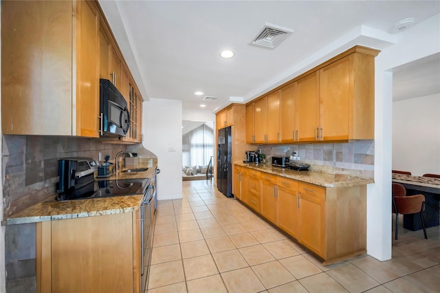 kitchen featuring light tile patterned floors, visible vents, light stone countertops, black appliances, and a sink