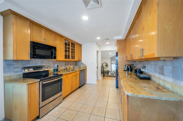 kitchen with stainless steel appliances, glass insert cabinets, light tile patterned flooring, a sink, and light stone countertops