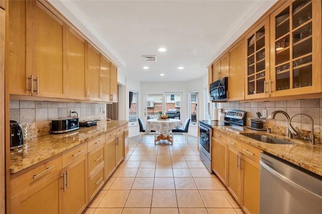 kitchen with a sink, visible vents, appliances with stainless steel finishes, light stone countertops, and glass insert cabinets