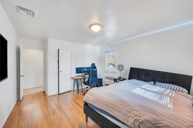 bedroom featuring radiator, light wood-type flooring, visible vents, and baseboards