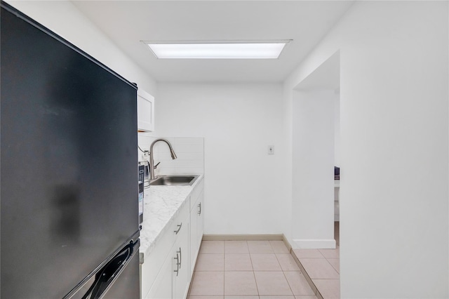 kitchen featuring light tile patterned flooring, a sink, freestanding refrigerator, and white cabinetry