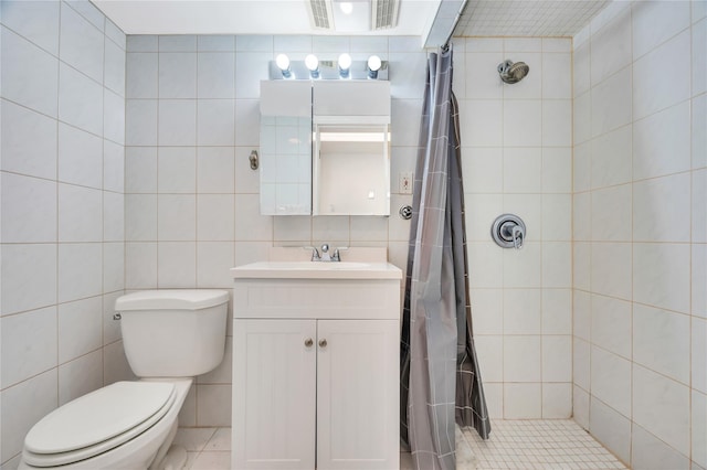 bathroom featuring visible vents, toilet, a tile shower, vanity, and tile walls