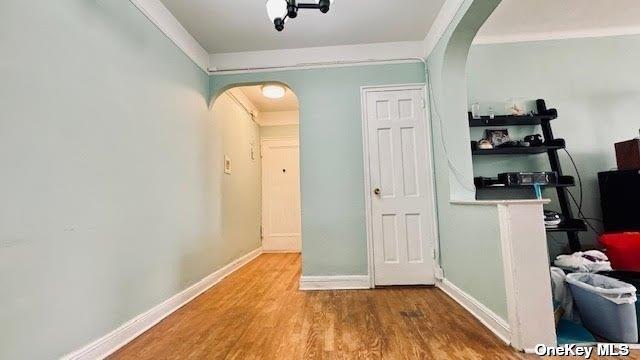 hall featuring baseboards, arched walkways, and wood finished floors