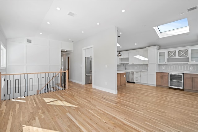 kitchen featuring wine cooler, light hardwood / wood-style flooring, stainless steel appliances, vaulted ceiling with skylight, and white cabinets