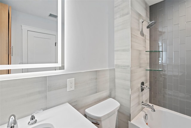 full bathroom with tile walls, sink, tiled shower / bath combo, and toilet