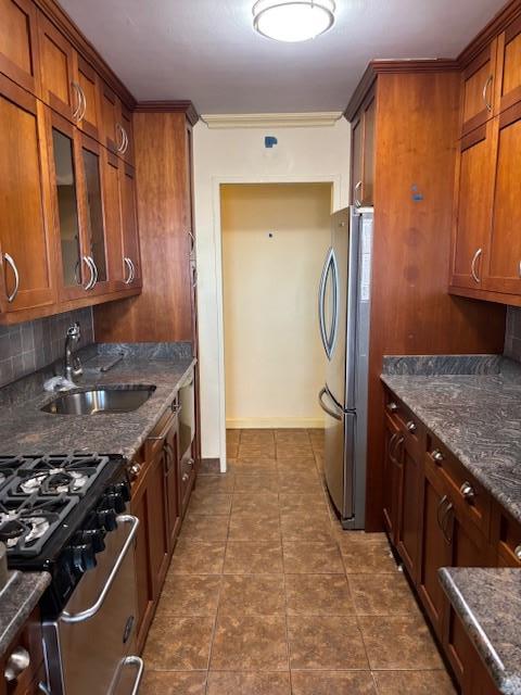 kitchen featuring decorative backsplash, glass insert cabinets, appliances with stainless steel finishes, brown cabinets, and a sink