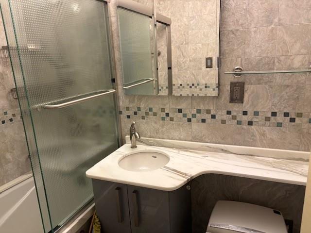 bathroom featuring bath / shower combo with glass door, tile walls, vanity, and decorative backsplash