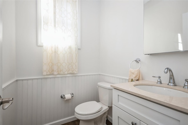 half bath featuring toilet, vanity, and wainscoting