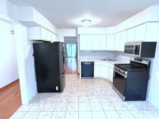 kitchen featuring appliances with stainless steel finishes, sink, white cabinets, backsplash, and light tile patterned floors