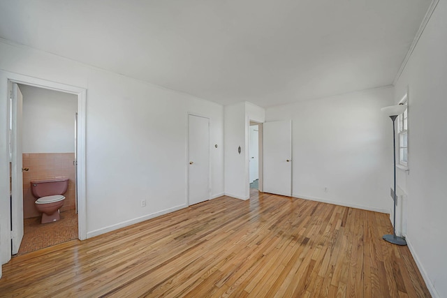 unfurnished bedroom with tile walls, light hardwood / wood-style flooring, and connected bathroom