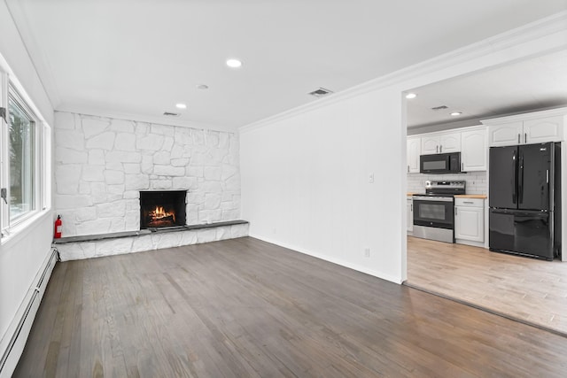 unfurnished living room with a fireplace, visible vents, baseboard heating, ornamental molding, and wood finished floors