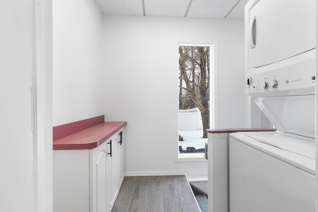 clothes washing area with cabinet space, baseboards, wood finished floors, and stacked washer and clothes dryer