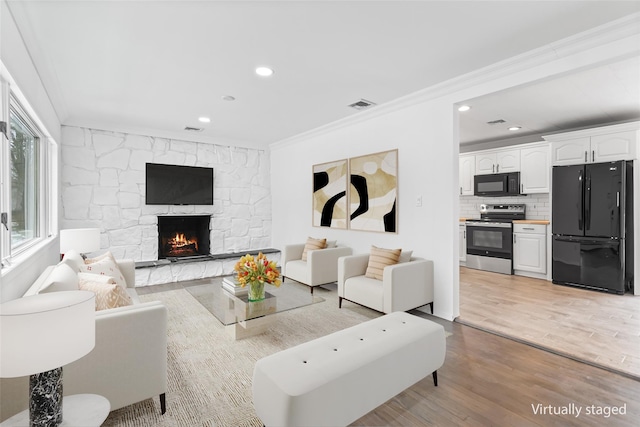 living area featuring ornamental molding, light wood-type flooring, visible vents, and a fireplace