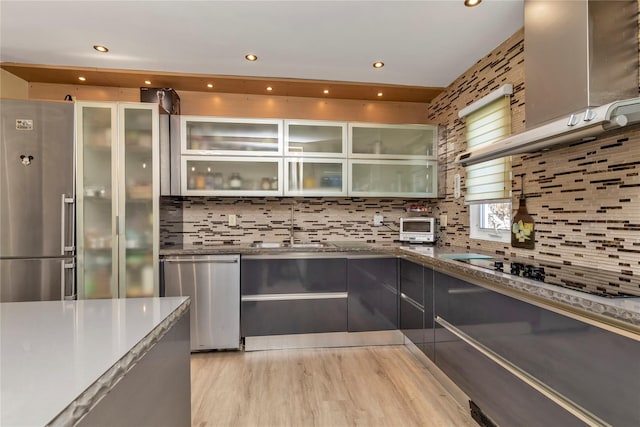 kitchen with a sink, dark stone counters, light wood finished floors, glass insert cabinets, and tasteful backsplash