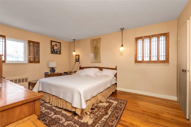 bedroom with radiator heating unit, light wood-type flooring, and baseboards