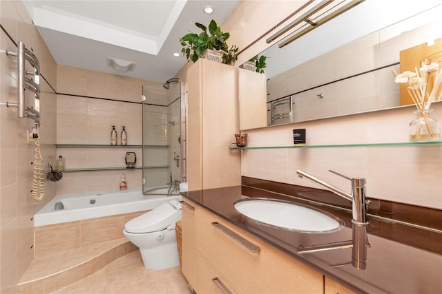 full bathroom with visible vents, toilet, tiled shower / bath, vanity, and tile walls