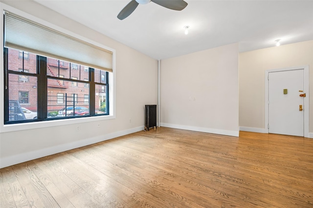 spare room featuring ceiling fan, radiator heating unit, and light hardwood / wood-style flooring