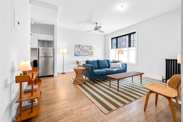 living room featuring baseboards, light wood finished floors, a ceiling fan, and radiator