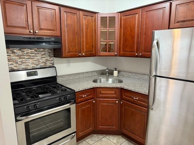 kitchen featuring sink, light stone counters, light tile patterned floors, stainless steel appliances, and backsplash