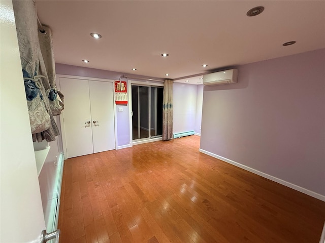 empty room featuring light wood finished floors, baseboards, a wall unit AC, baseboard heating, and recessed lighting