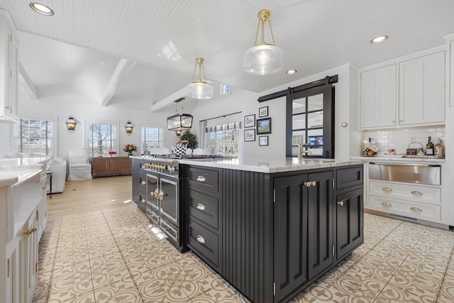 kitchen with a barn door, a kitchen island with sink, white cabinetry, open floor plan, and a warming drawer