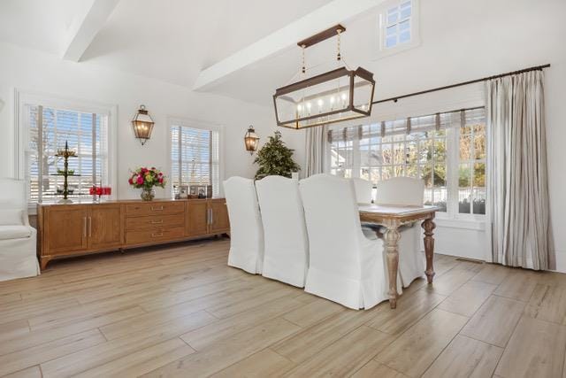 dining room with light wood-type flooring, a wealth of natural light, a chandelier, and beamed ceiling