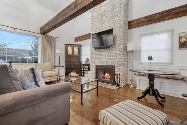 living area featuring high vaulted ceiling, beam ceiling, a fireplace, and wood finished floors