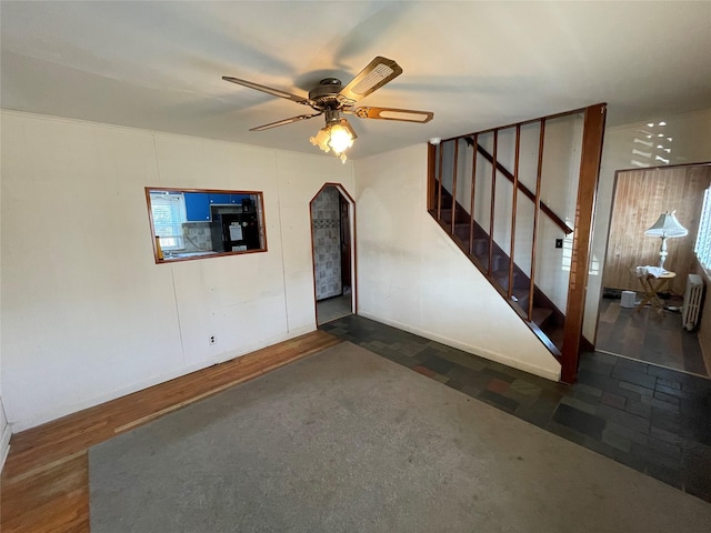 interior space featuring arched walkways, dark wood finished floors, radiator heating unit, ceiling fan, and stairway