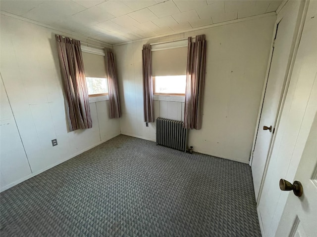 unfurnished room featuring dark colored carpet and radiator heating unit