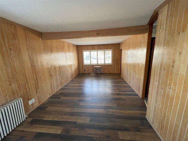 empty room featuring wooden walls, dark wood finished floors, beam ceiling, and radiator