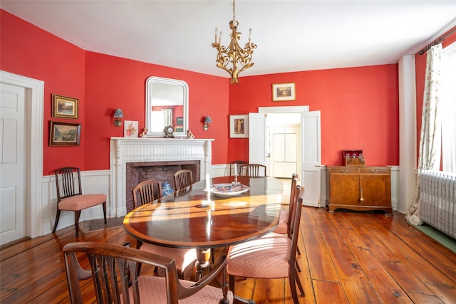 dining room with a fireplace, radiator, an inviting chandelier, and wood-type flooring