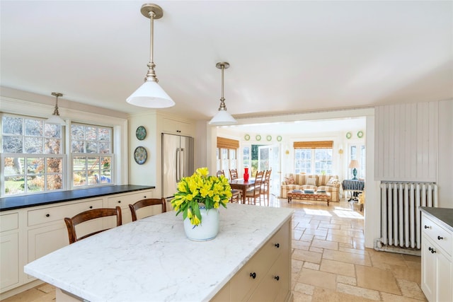 kitchen with dark stone counters, a kitchen island, decorative light fixtures, stainless steel refrigerator, and radiator