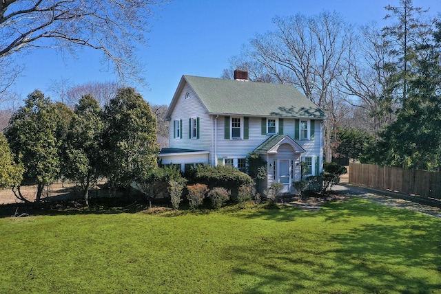 colonial inspired home featuring roof with shingles, a chimney, a front yard, and fence