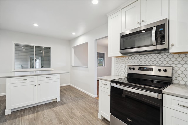 kitchen with appliances with stainless steel finishes, light wood-type flooring, white cabinets, and backsplash