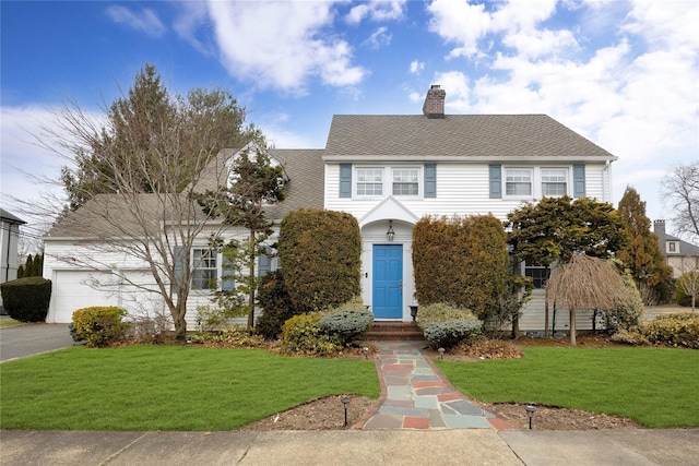 colonial house featuring driveway, a chimney, a front lawn, and roof with shingles