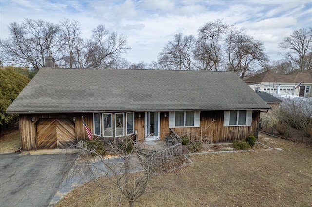 view of front of home featuring a garage, driveway, a shingled roof, and a chimney