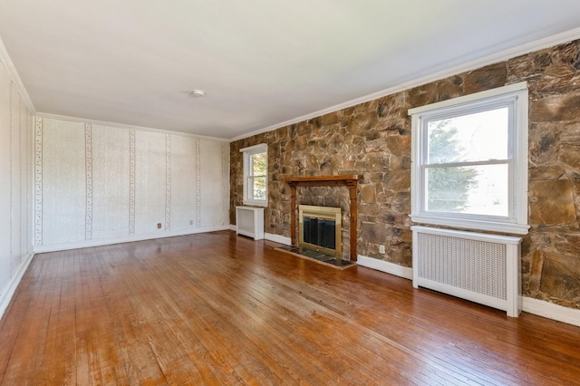 unfurnished living room with hardwood / wood-style floors, a fireplace, ornamental molding, and radiator