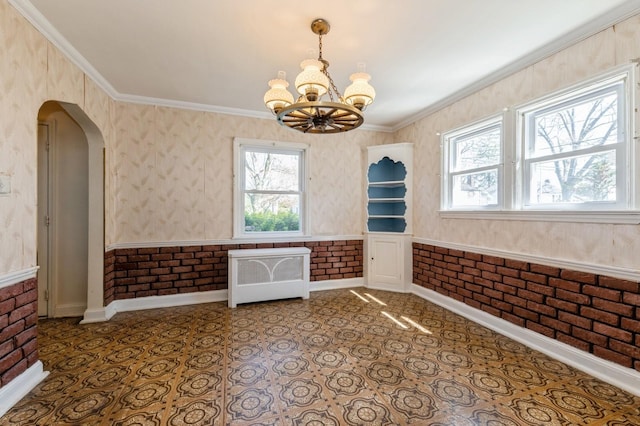 unfurnished dining area featuring radiator heating unit, arched walkways, crown molding, baseboards, and a chandelier