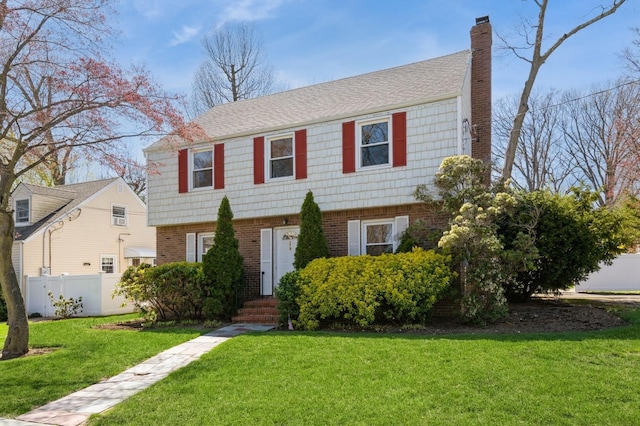colonial inspired home featuring a chimney, brick siding, fence, and a front yard