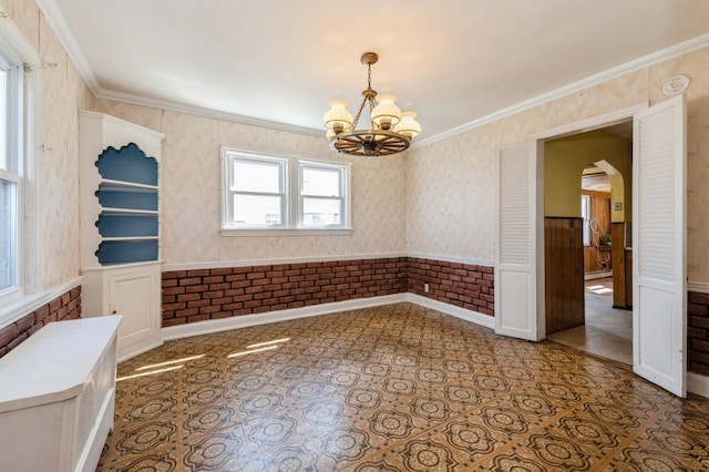 spare room with wainscoting, arched walkways, an inviting chandelier, and ornamental molding