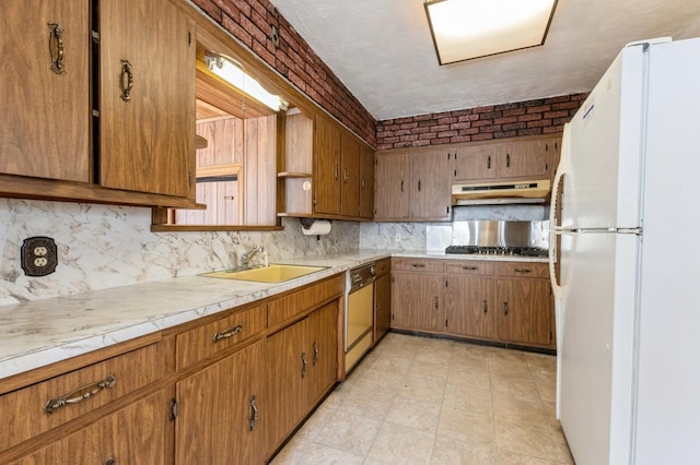 kitchen featuring light countertops, a sink, freestanding refrigerator, dishwasher, and under cabinet range hood