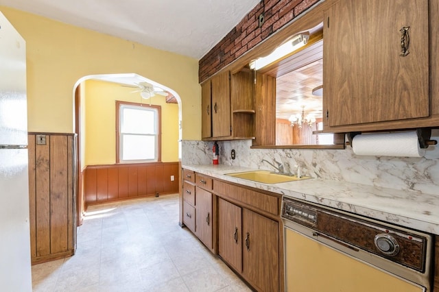 kitchen with a wainscoted wall, light countertops, dishwashing machine, a sink, and arched walkways