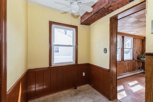 empty room featuring a baseboard heating unit, wooden walls, a wainscoted wall, and a ceiling fan