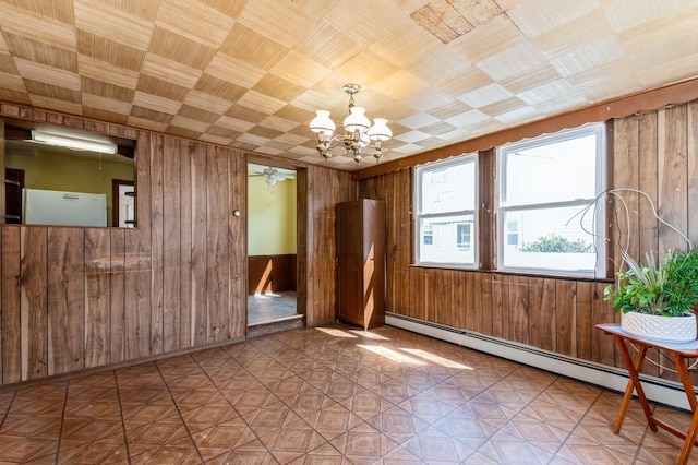 unfurnished room featuring baseboard heating, wood walls, and an inviting chandelier