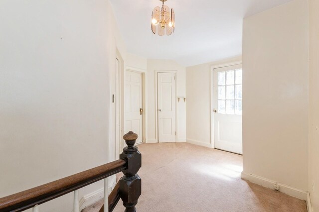 corridor with carpet floors, a chandelier, and baseboards