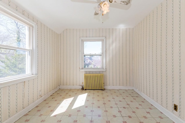 spare room featuring radiator heating unit, plenty of natural light, a ceiling fan, and light floors