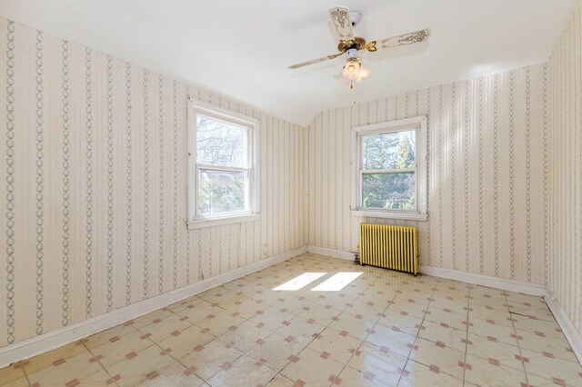 empty room with plenty of natural light, a ceiling fan, tile patterned floors, and radiator