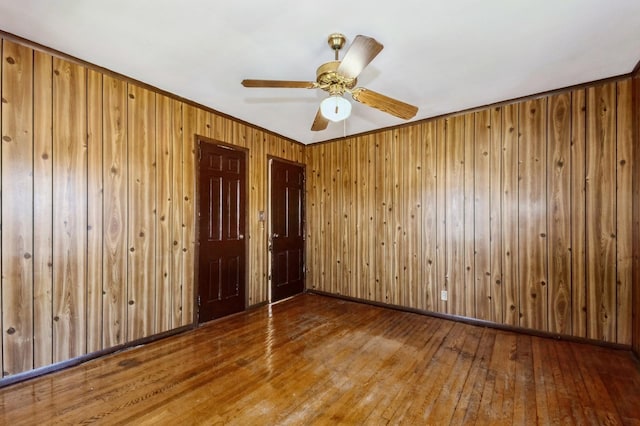 unfurnished room with hardwood / wood-style flooring, ceiling fan, baseboards, and wooden walls