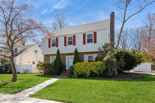 colonial house with fence, a front lawn, a chimney, and brick siding